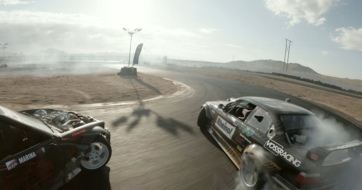 Two black drift cars sliding door-to-door through tire smoke