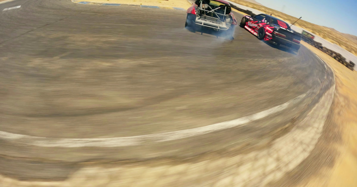 Two drift cars with exposed roll cages exiting a corner together